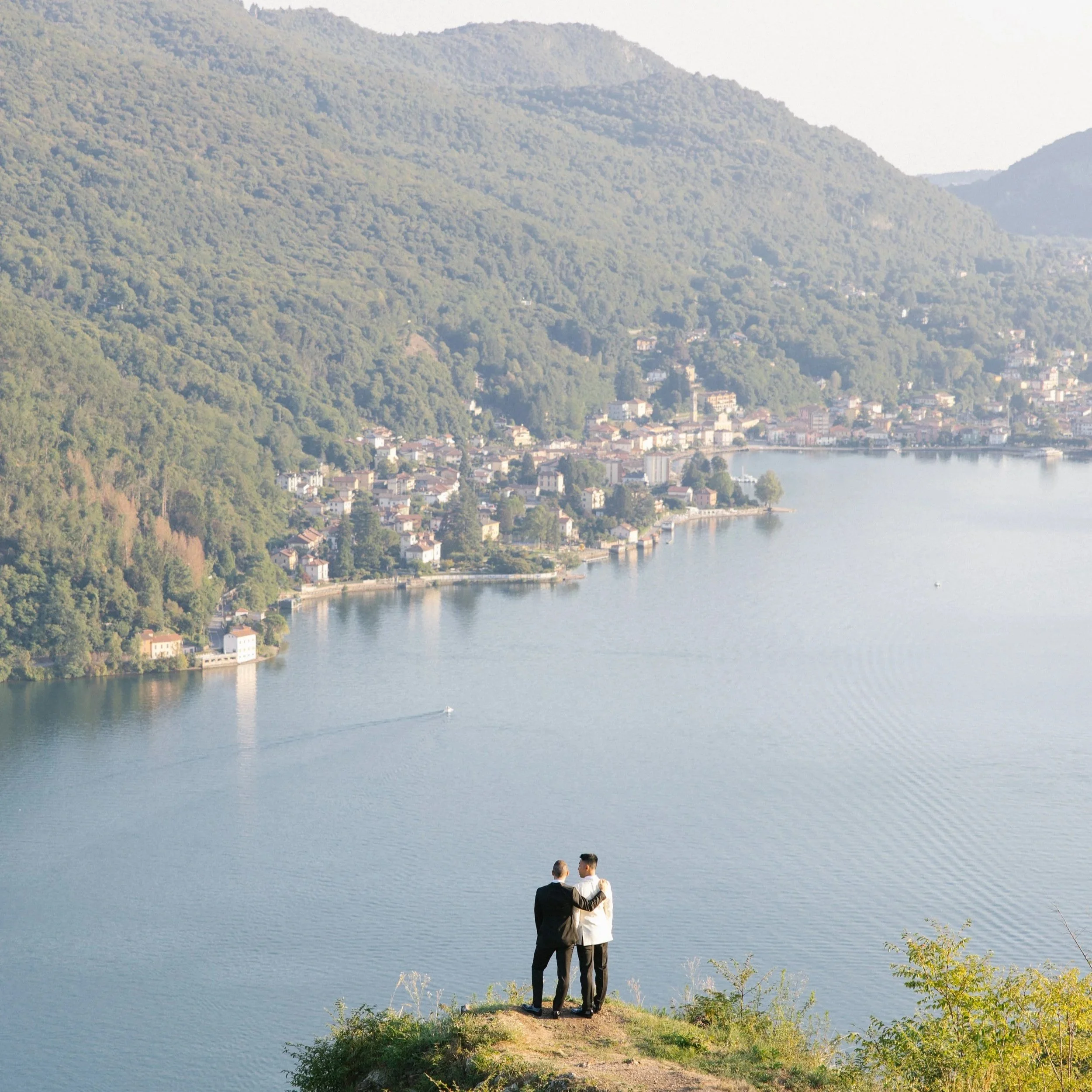 Daniel and Hafi in wedding suits, looking out over a lake and wooded hills